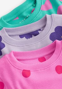 Tre T-shirts staplade: en tealtröja med rosa former, en lavendelfärgad tröja med lila blommor och en rosa tröja med röda prickar. Bomullstyg.