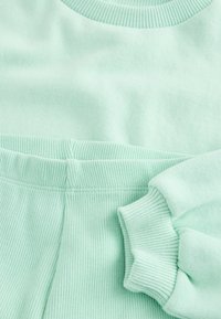 Sudadera de punto acanalado en verde menta y pantalones a juego, mostrando el cuello redondo, la cintura elástica y los detalles de los puños en las mangas.
