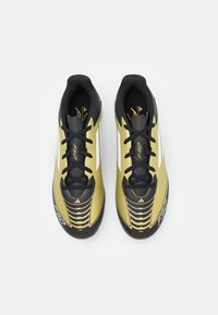 Scarpe da calcio oro e nere con una finitura sintetica liscia, caratterizzate da un design elegante, dettagli testurizzati e lacci neri.