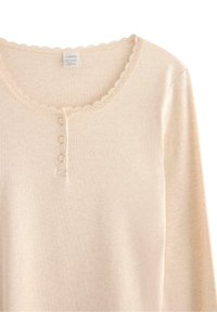Cremefarvet ribbet langærmet top med scallop-lace halsudskæring og tre små knapper på fortil.