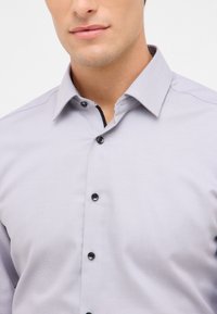 Lichtgrijze button-up shirt gemaakt van gestructureerde stof, met een normale kraag, zwarte knopen en een contrasterend detail aan de binnenkant van de kraag.