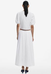 Witte gekorte top met pofmouwen, gecombineerd met een witte maxi rok met een elastische tailleband; gedragen met blauwe hoge hakken.