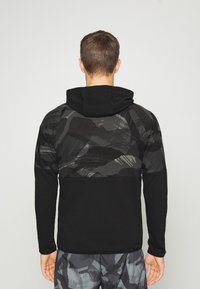Sudadera negra con un patrón de camuflaje gris texturizado en la parte trasera y los hombros. Mangas largas y un diseño ajustado. Tejido suave con capucha.