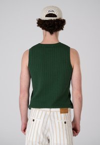 Green ribbed tank top with wide armholes and a round neckline, paired with beige and white striped pants, seen from the back.