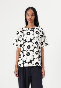 Korte ermertopp laget av myk stoff med et svart-hvitt blomsterdesign, rund halslinning og løs passform.