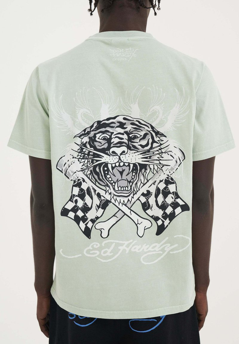 Camiseta de manga corta verde claro con un gran gráfico de tigre negro, banderas a cuadros cruzadas y el texto "Ed Hardy" en blanco.