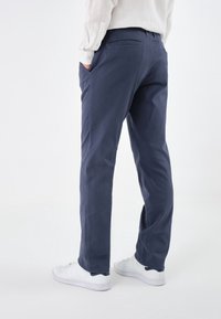 Pantaloni di cotone blu navy con taglio dritto, due tasche laterali e una tasca posteriore, abbinati a sneakers bianche. Texture liscia.