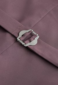Un tissu violet avec une texture lisse présente un fermoir métallique. Des détails de couture en rose complètent le design.