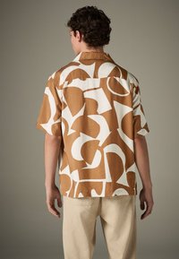 Trumpomis rankovėmis marškiniai su rudai baltu abstrakčiu raštu, pagaminti iš lengvos medžiagos, laisvo silueto.