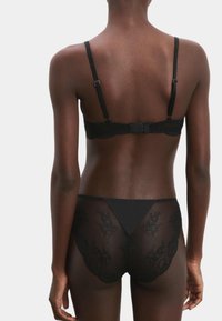Ensemble de lingerie en dentelle noire comprenant un bralette avec des bretelles ajustables et une fermeture à crochet, associé à un slip taille haute transparent.