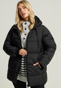 Doudoune noire avec capuche, dotée d'une fermeture éclair à l'avant, de cordons de serrage réglables et de poches latérales. Portée par-dessus un pull rayé gris.