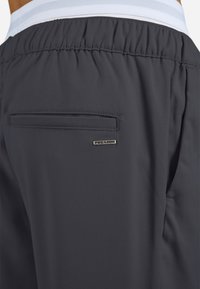 Sötétszürke sportos rövidnadrág texturált anyagból, rugalmas derékrésszel és oldalzsebbel. Látható a "PEGADOR" márkalogó.