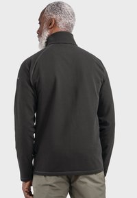 Dunkelgraue Fleecejacke mit hohem Kragen und langen Ärmeln. Glatte Textur, kontrastierende Nähte und ein Logo auf der Schulter.