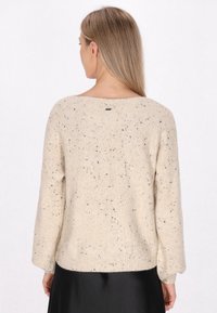 Beżowy sweter dzianinowy z czarnymi plamkami. Posiada szeroki dekolt, luźne rękawy i prążkowany dół. Metka widoczna z tyłu. Gładka tekstura.