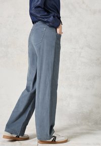 Ljusblå vida byxor i mjukt tyg, med bakfickor, detaljerad sömnad och bärs med vita skor och en mörk skjorta.