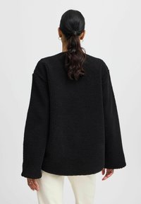 Svart fleecejacka med en texturerad yta, oversized passform, nedhängda axlar och långa ärmar. Ingen synlig hårdvara eller mönster.