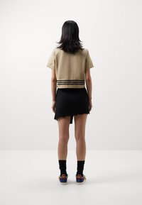 Zkrácený béžový top s krátkým rukávem, černá plisovaná mini sukně s roztrhaným lemem a klasické tenisky s vícebarevnými akcenty.