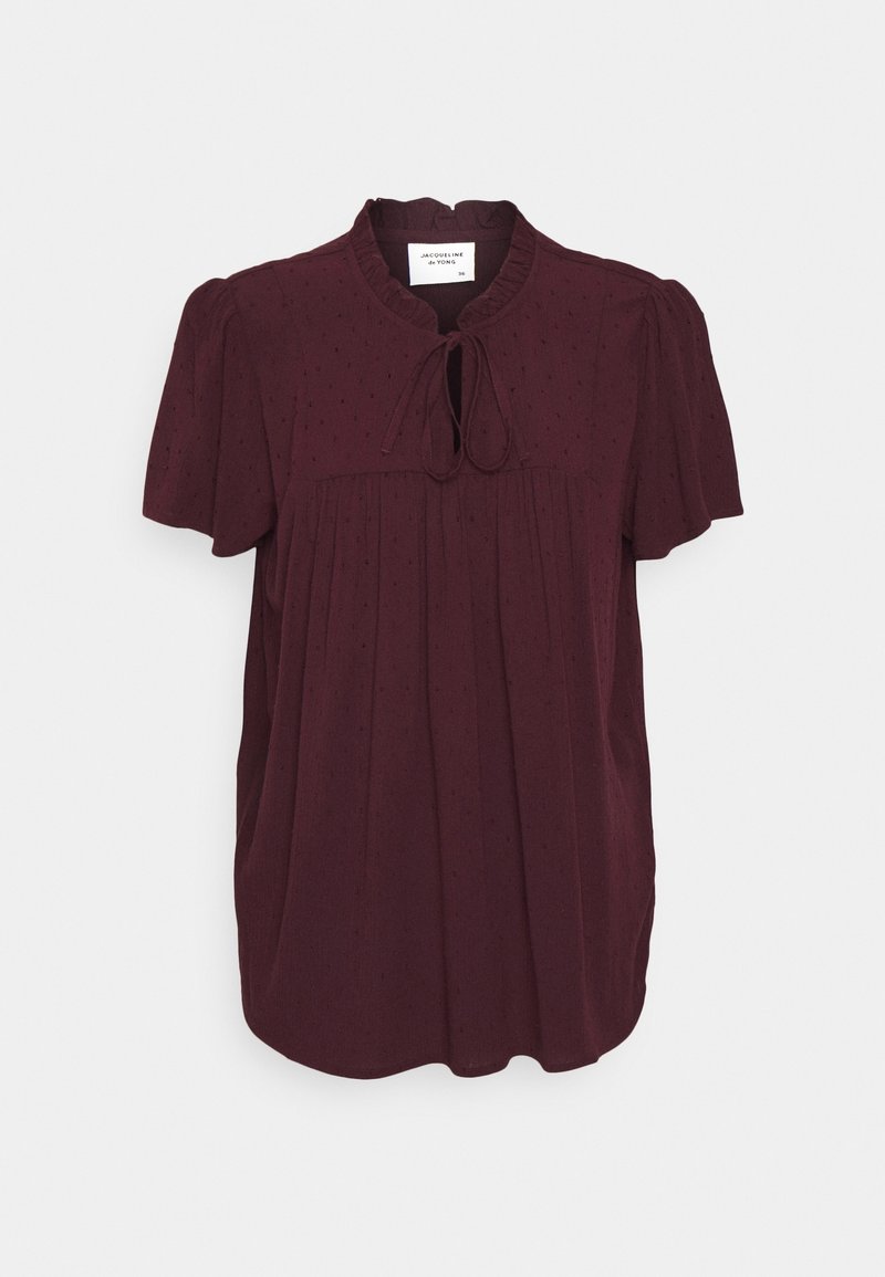 Blouse manches courtes bordeaux foncé avec motif à pois texturé, col volanté et détail noué à l'avant, présentée sur fond uni.