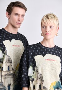 Sorte grafiske t-shirts med kunstneriske tryk af arkitektoniske elementer og kort. Inkluderer teksten "CARLO COLOUCCI" i rødt.