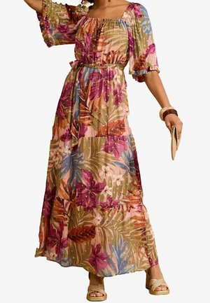 Femme portant une robe maxi fleurie ceinturée avec des manches bouffantes, tenant une pochette beige, et portant des sandales à talons blocs tissés ainsi que des bracelets.
