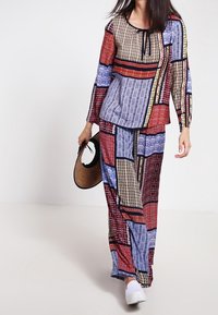 Outfit multicolore con motivi geometrici in rosso, blu e crema. Maniche lunghe sulla parte superiore, pantaloni a gamba larga e una borsa rotonda.