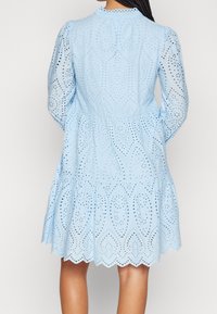 Blå ögla klänning med långa ärmar, en figursydd midja och lager på lager kjol, med intrikata utskärningsmönster och vågig fåll.