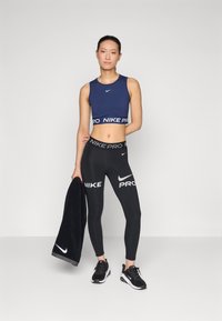 Marinefarget, cropped sports-top med hvit Nike-logo, kombinert med svarte leggings med dristig "Nike Pro" branding og et matchende svart håndkle.