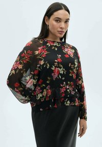 Blusa nera floreale con maniche lunghe trasparenti e orlo arricciato, caratterizzata da motivi floreali multicolori in rosso, rosa e verde.