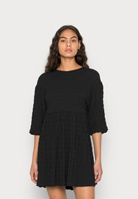 Vestido preto, texturizado, de mangas curtas e corte descontraído, com corpete franzido, apresentando pregas horizontais e decote redondo.