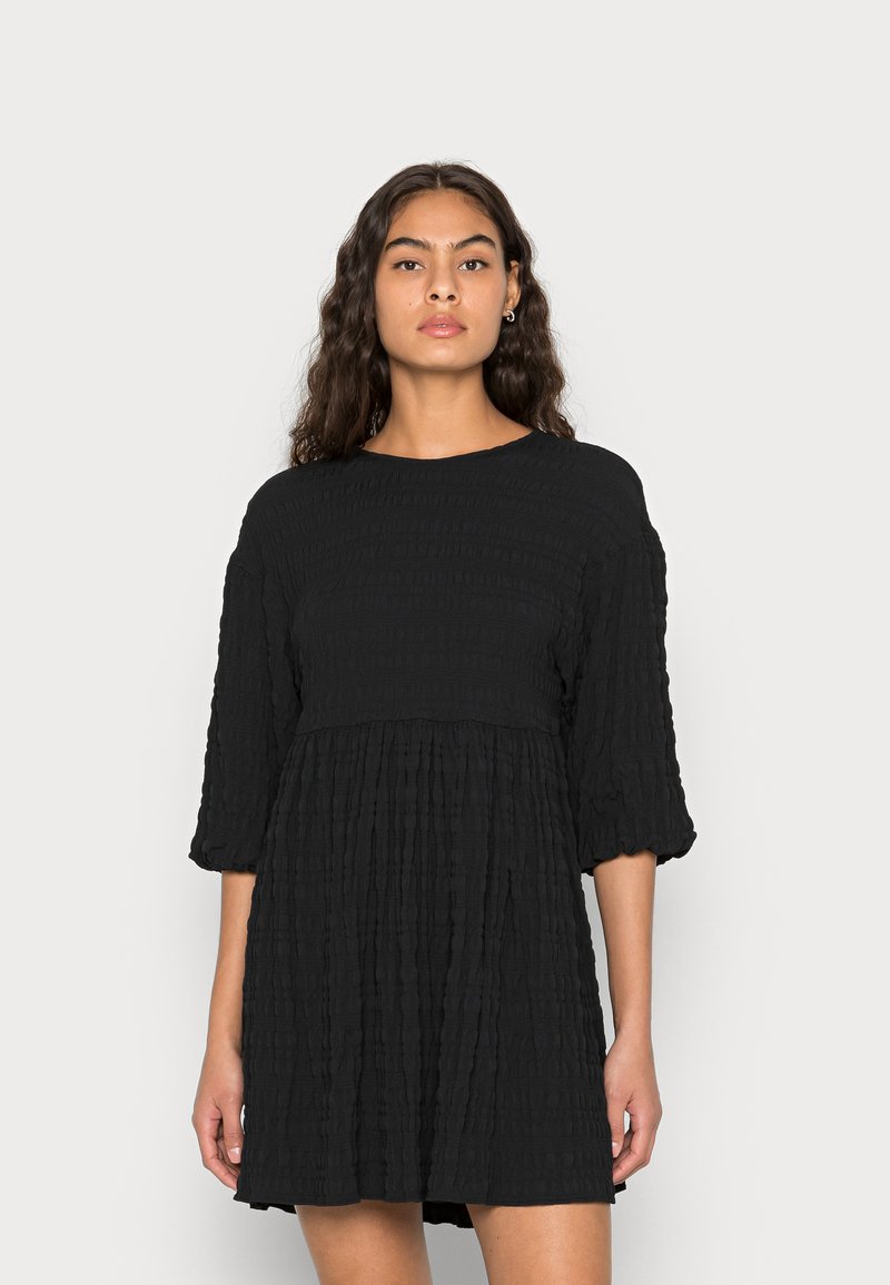 Vestido preto, texturizado, de mangas curtas e corte descontraído, com corpete franzido, apresentando pregas horizontais e decote redondo.