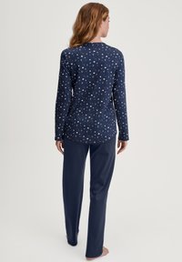 Completo pigiama in blu navy, composto da una maglietta a maniche lunghe con motivo celestiale e pantaloni in tinta unita. Tessuto morbido con vestibilità rilassata; design senza etichetta.