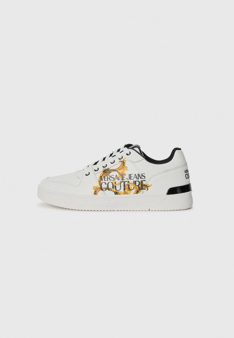 Sapatilhas brancas de couro com detalhes em preto. Apresentam padrões florais dourados e a inscrição "VERSACE JEANS COUTURE" na lateral e no calcanhar.
