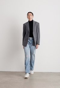 Grå blazer over svart turtleneck, lyseblå slitte jeans og hvite sneakers. Glatt stoff, strukturert design og avslappet passform.