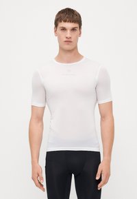 Chemise de performance blanche ajustée à manches courtes, en tissu texturé, avec un col arrondi et un logo subtil sur la poitrine, associée à un bas noir.