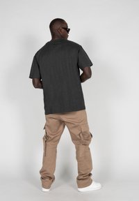 Graues Baumwoll-T-Shirt mit kurzen Ärmeln, kombiniert mit tanfarbenen Cargo-Hosen mit mehreren Taschen und weißen Sneakers, von hinten betrachtet.