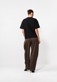 Czarny krótki rękaw oversize t-shirt w połączeniu z brązowymi spodniami o szerokich nogawkach. T-shirt ma okrągły dekolt i luźny krój.