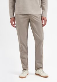 Lichtbeige chino's met een gladde textuur, slim fit en steekzakken. Draagt met witte sneakers met een lichtbruine zool.