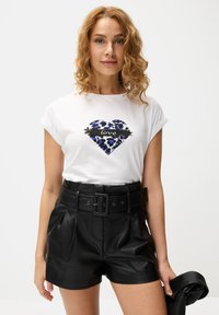 Weißes T-Shirt mit einem blauen und schwarzen Leopardenherz, auf dem das Wort "love" in Schwarz geschrieben ist, kombiniert mit hochgeschnittenen schwarzen Leder-Shorts.