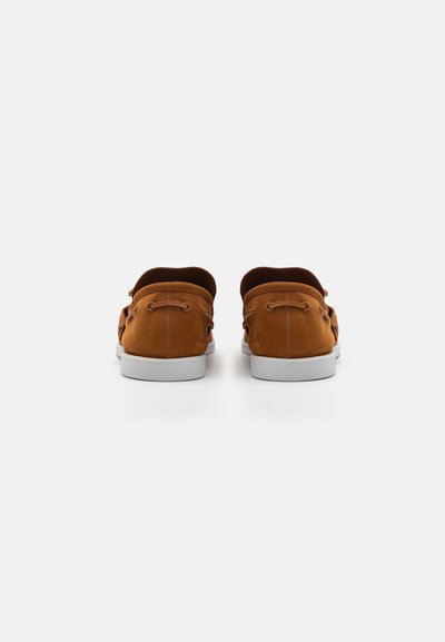 Brown suede casual shoes with a low profile, white rubber soles, and lacing detail at the back. Smooth texture and rounded shape.