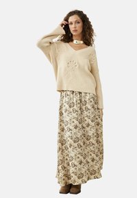 Suéter de punto beige con textura de canalé y bordado floral, combinado con una falda larga color crema con patrones florales marrones y botas marrones.