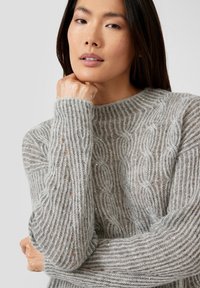 Hellgrauer Strickpullover mit Zopfmuster, gerippter Struktur und dezenten silbernen Sprenkeln. Rundhalsausschnitt und lange Ärmel mit Knopfakzenten.