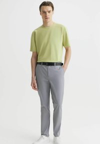 Jasnozielona koszulka polo z krótkim rękawem zestawiona z szarymi spodniami i białymi trampkami. Smukły, nowoczesny krój z czarnym paskiem. Miękka tekstura, minimalistyczny design.