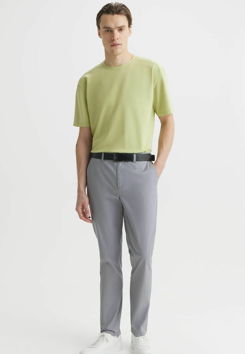 Jasnozielona koszulka polo z krótkim rękawem zestawiona z szarymi spodniami i białymi trampkami. Smukły, nowoczesny krój z czarnym paskiem. Miękka tekstura, minimalistyczny design.