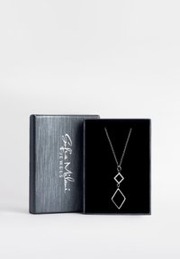 Silverhalsband med två geometriska hängen, ett med kontur och det andra prytat med stenar, visat i en svart sammetask.