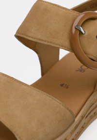 Ταμπά σουέντ σανδάλι με δύο φαρδιές λουρίδες και μια μεγάλη καφέ κυκλική αγκράφα. Τακούνι πλατφόρμα από φελλό με υφή και μέγεθος σημειωμένο στο εσωτερικό.