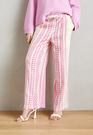 Pantaloni a gamba larga color crema con motivi geometrici rosa, tessuto testurizzato e vita con laccetto. Abbinati a sandali bianchi con tacco.