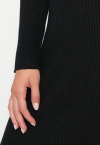 Mano sinistra con unghie naturali appoggiata su una manica di abbigliamento in tessuto a coste nero.