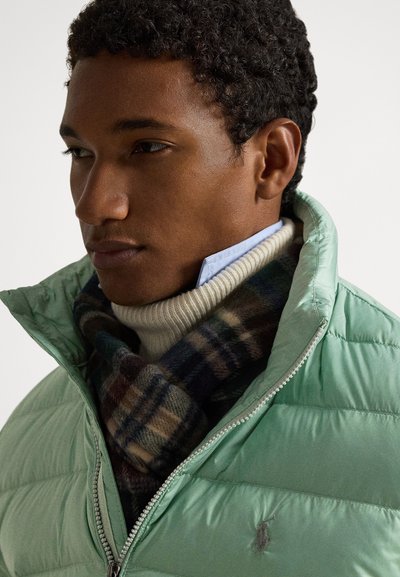 Svetlozelená nadýchaná bunda so zapínaním na zips vpredu, vrstvená cez krémový rolák a károvaný šál s tmavomodrými, zelenými a hnedými tónmi.