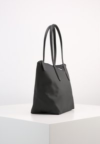 Schwarze Tasche mit strukturiertem Oberflächen, zwei langen Griffen und einem Reißverschluss. Das Design ist minimalistisch und strukturiert.