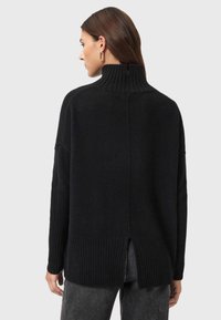 Suéter negro de punto con cuello alto, dobladillo acanalado y detalles de abertura lateral. Textura suave, corte oversize y mangas largas.